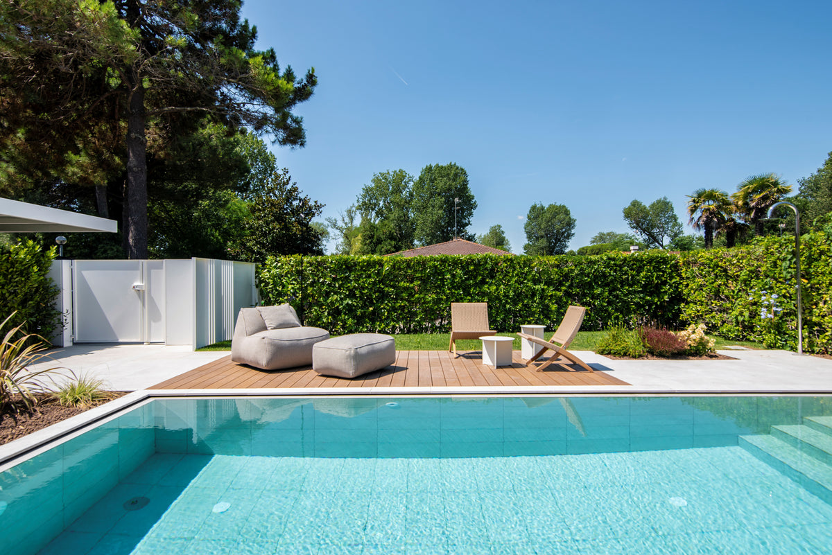 Piscina con solarium in legno e sedute lounge immerse nel verde del giardino