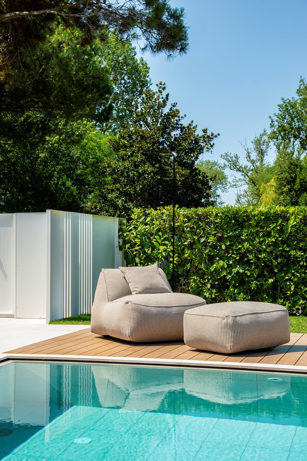 Chaise longue con pouf GART sul deck in legno accanto alla piscina e al giardino