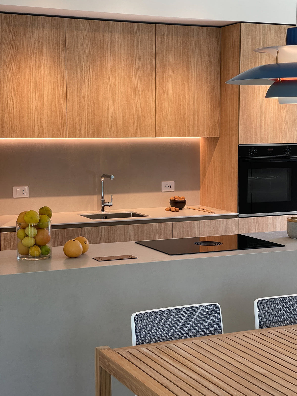 Cucina contemporanea su misura con arredi in legno, isola centrale, piano chiaro e illuminazione integrata