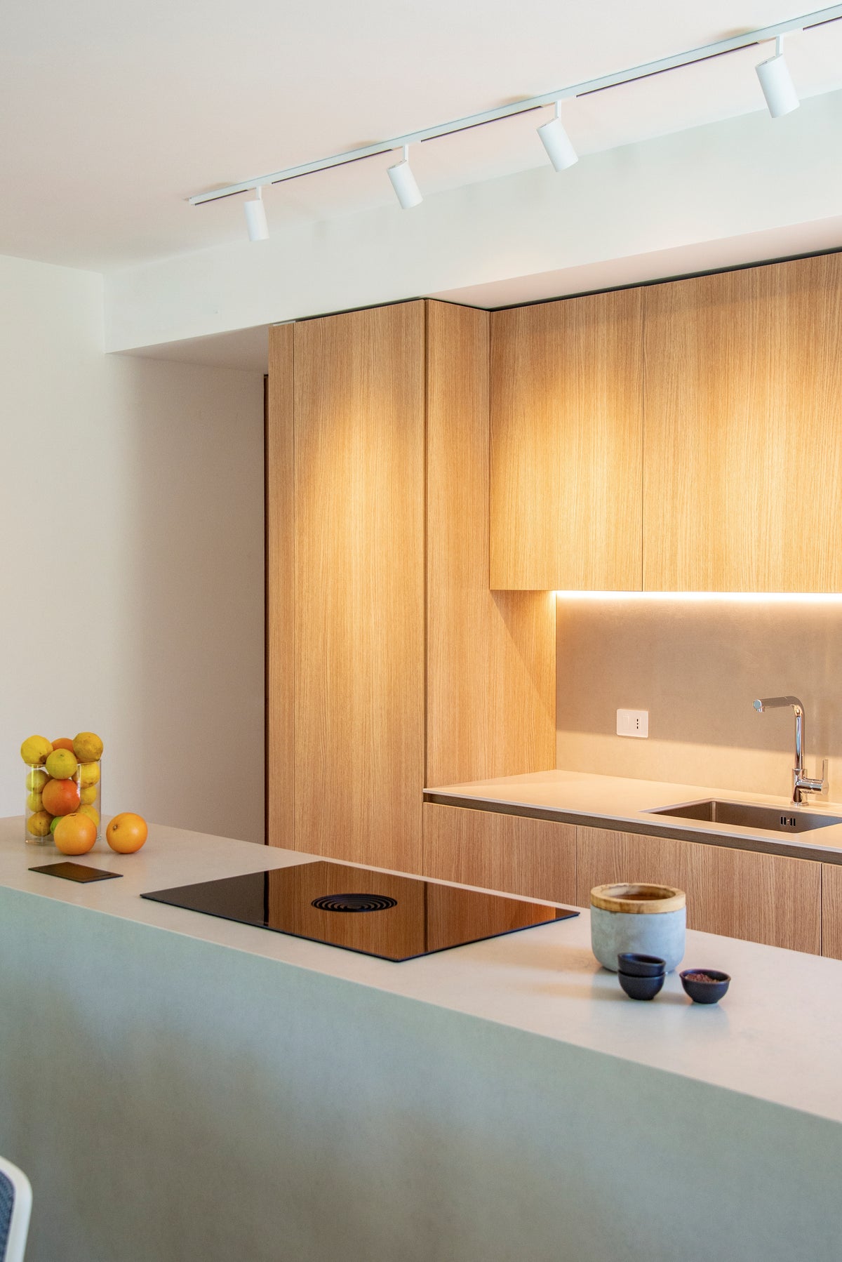Dettaglio della cucina su misura con isola chiara, ante in legno e illuminazione integrata