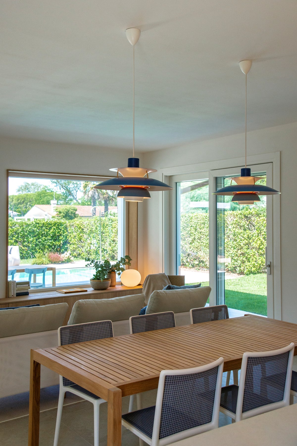 Zona pranzo e living con grandi aperture vetrate verso giardino e piscina