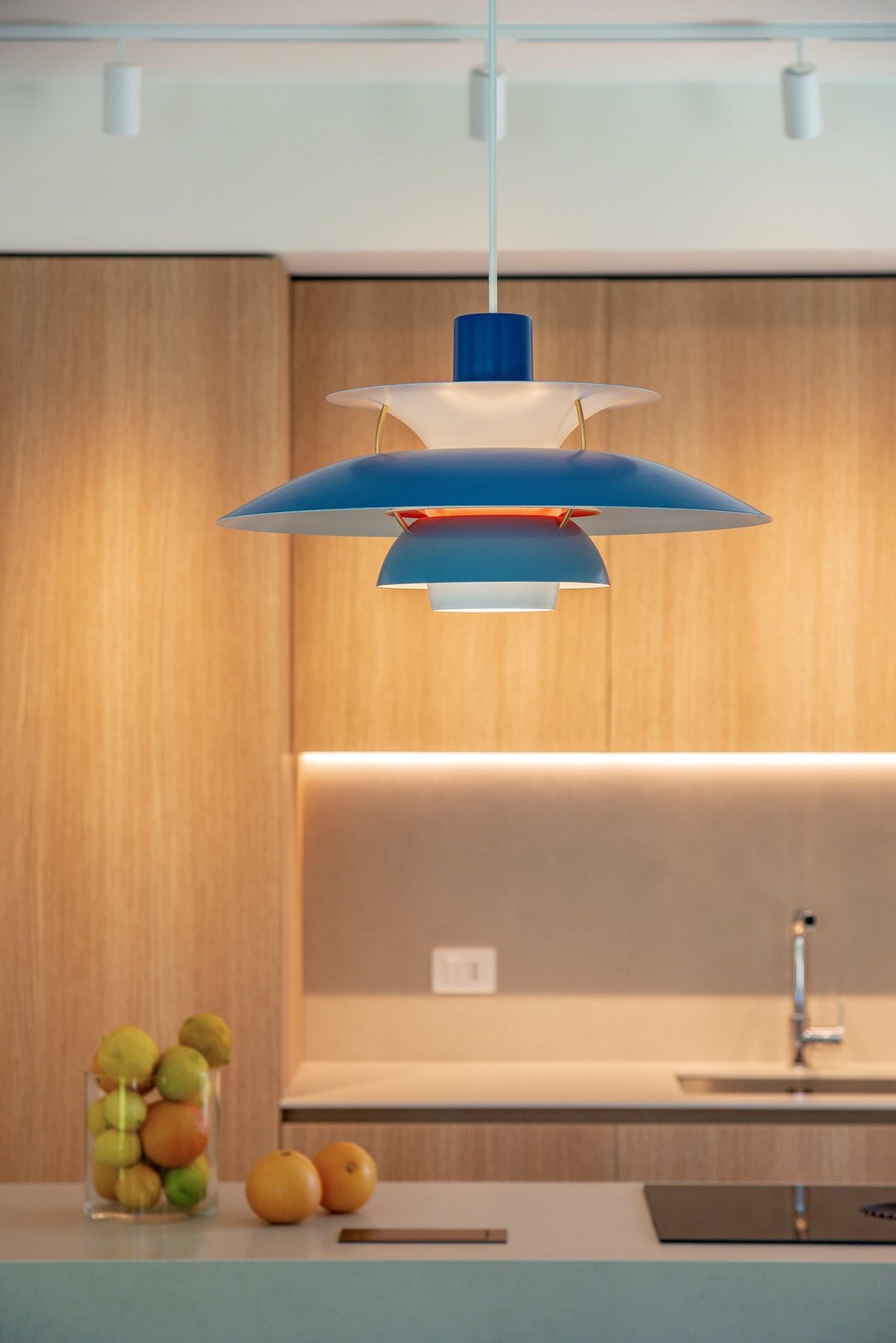 Dettaglio della lampada a sospensione sopra la zona pranzo con cucina in legno sullo sfondo