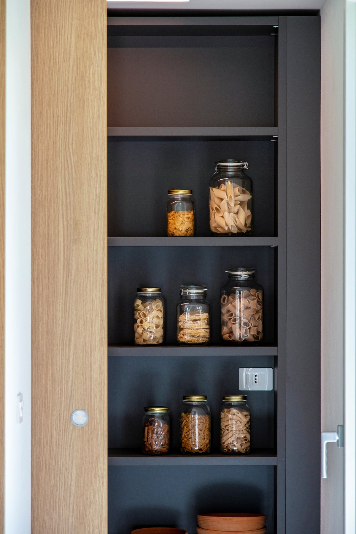 Dispensa integrata nella cucina con scaffali scuri e contenitori a vista