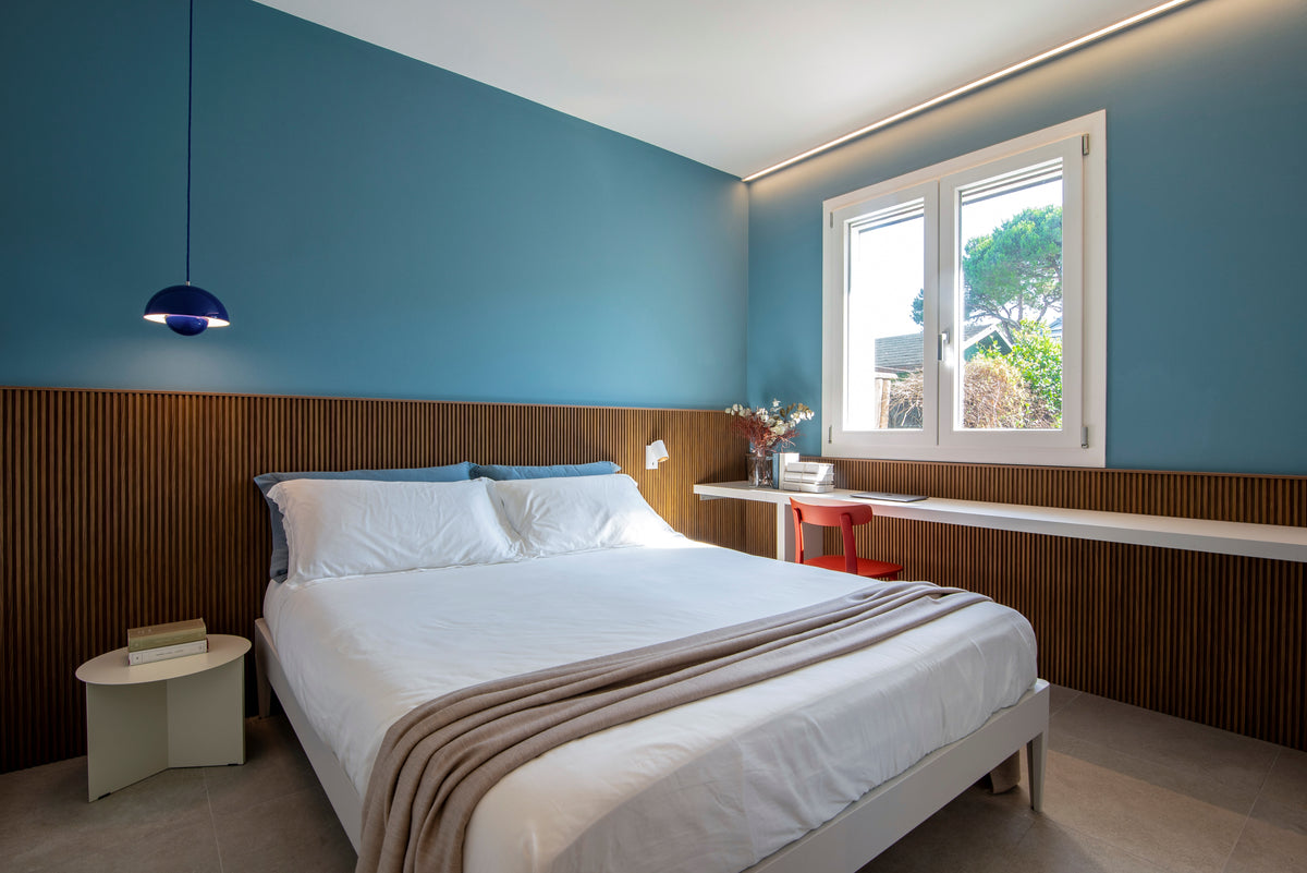 Camera da letto della casa ristrutturata ad Albarella con boiserie in legno, pareti azzurre e scrittoio su misura sotto la finestra