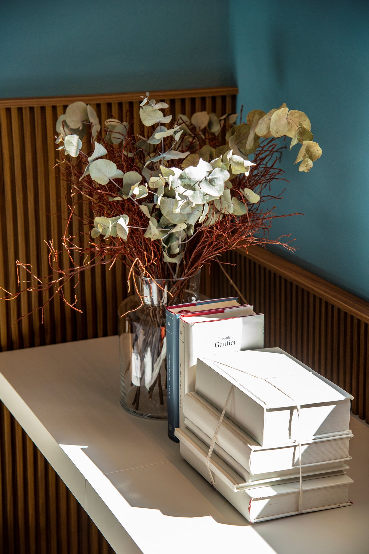 Dettaglio dello scrittoio con libri e composizione floreale davanti alla boiserie verticale in legno