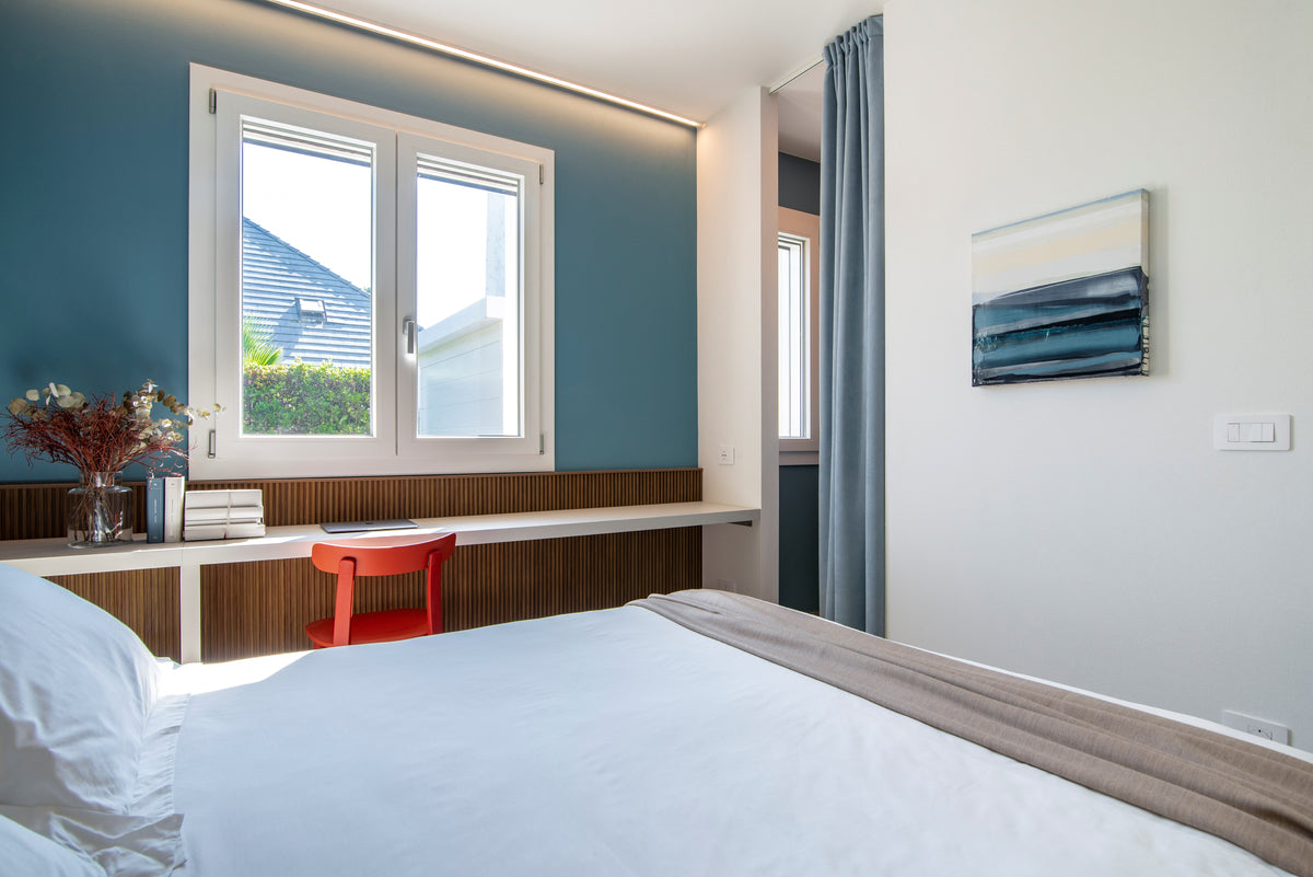 Camera luminosa con letto, scrittoio su misura, parete azzurra e tenda che separa la zona guardaroba