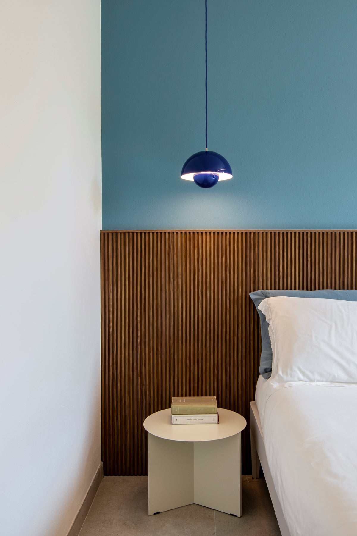 Dettaglio del comodino con lampada a sospensione blu e boiserie retro letto in legno