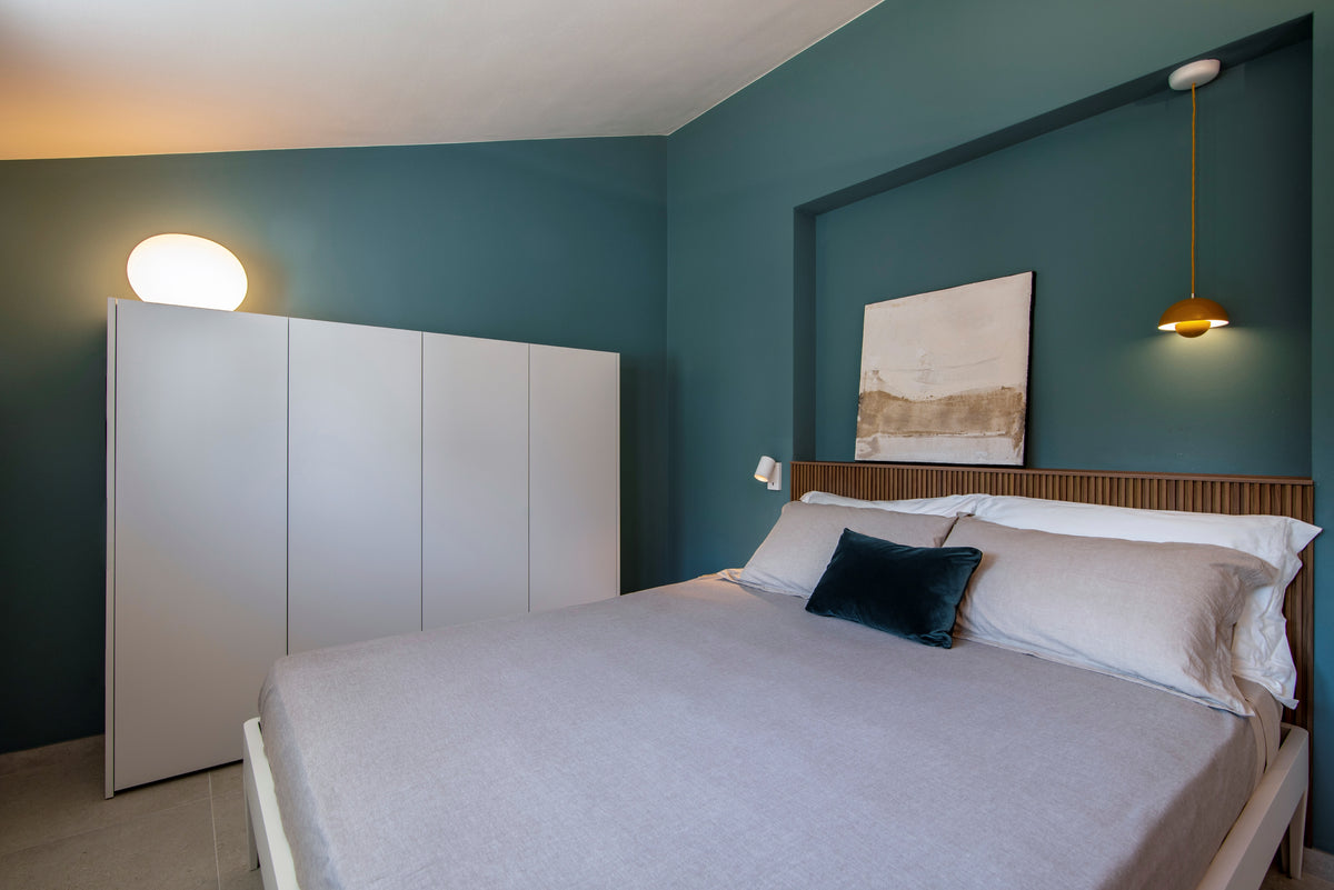 Camera con letto, armadio bianco, boiserie in legno e lampada a sospensione su parete blu