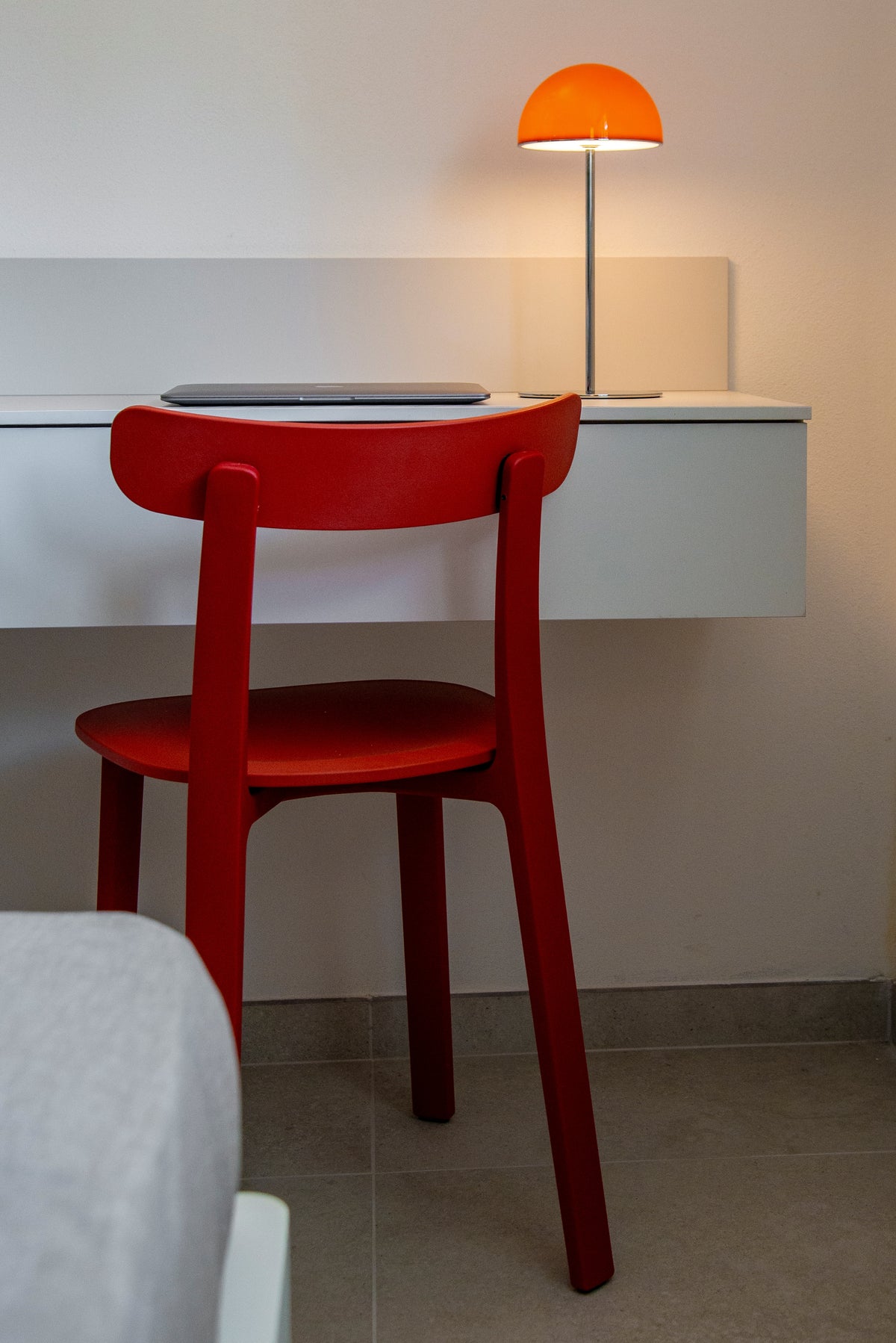 Dettaglio dello scrittoio sospeso con sedia rossa e lampada da tavolo arancione