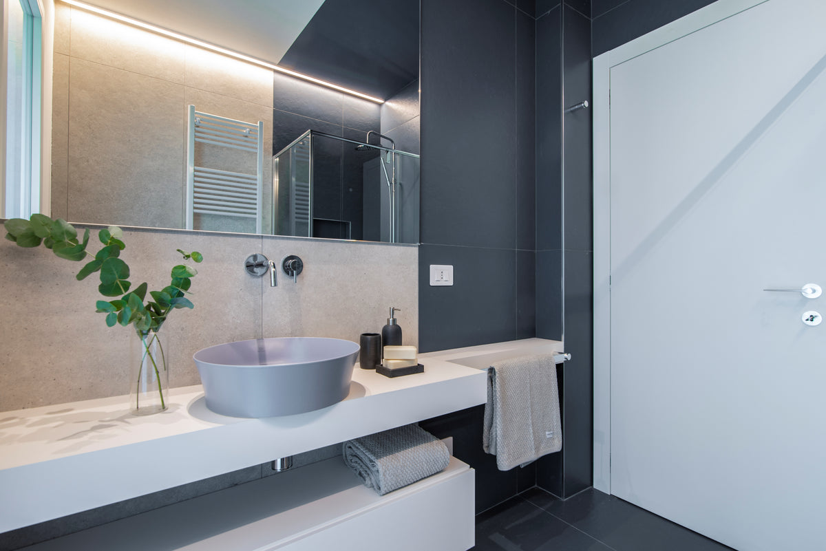 Bagno della casa ristrutturata ad Albarella con lavabo da appoggio, mobile sospeso, grande specchio e rivestimenti grigio antracite