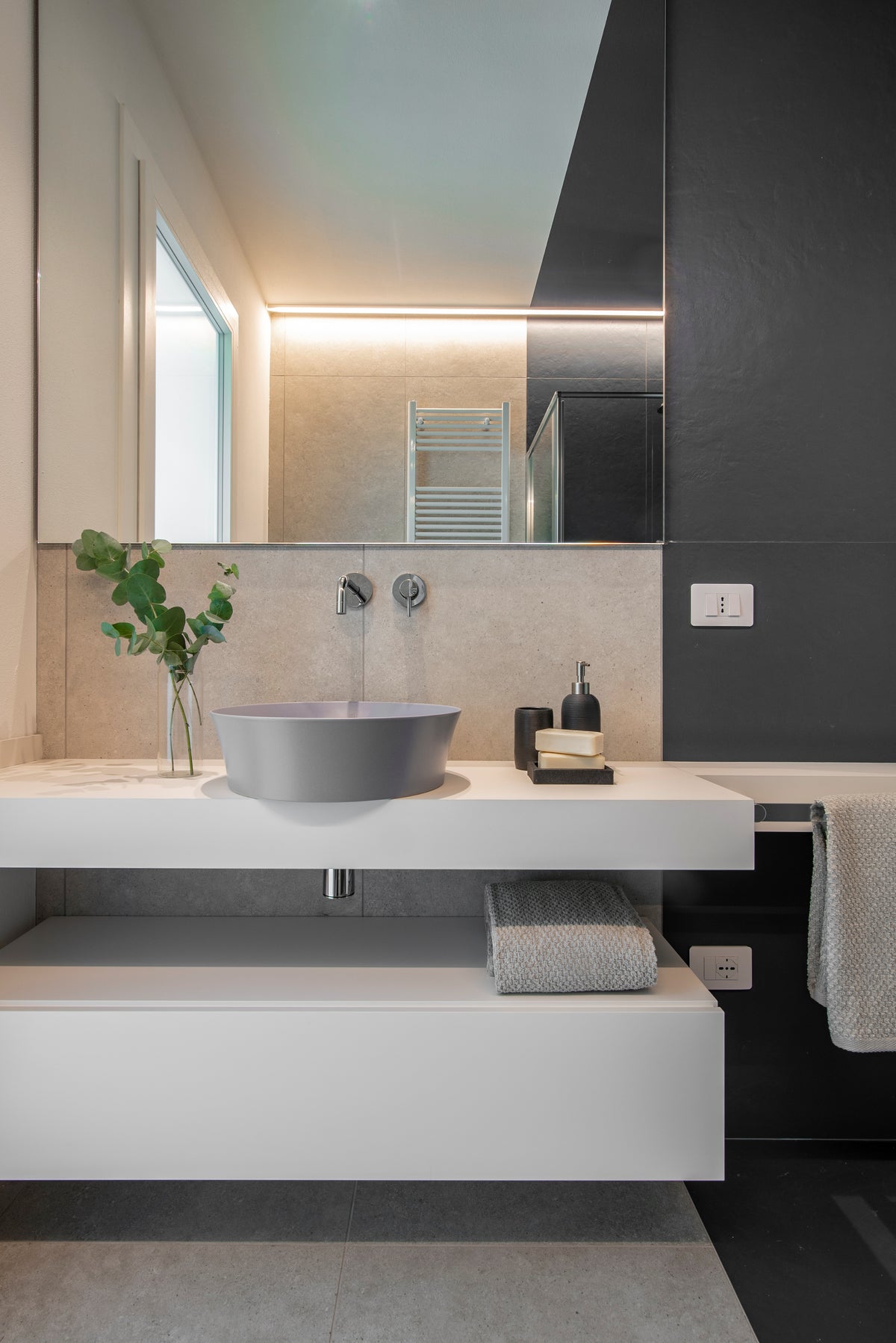 Dettaglio del bagno con lavabo da appoggio grigio, piano sospeso bianco e specchio a tutta parete