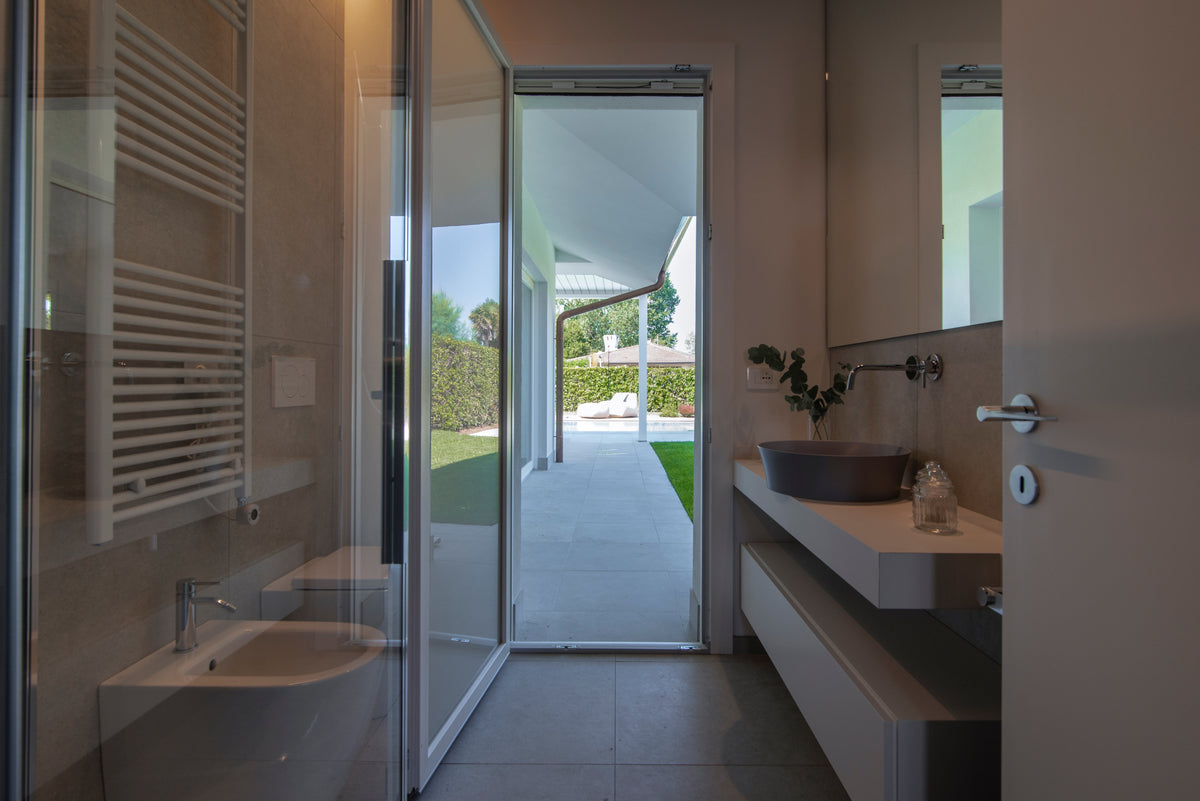 Bagno con doccia in vetro, sanitari sospesi e mobile lavabo affacciato direttamente sul giardino