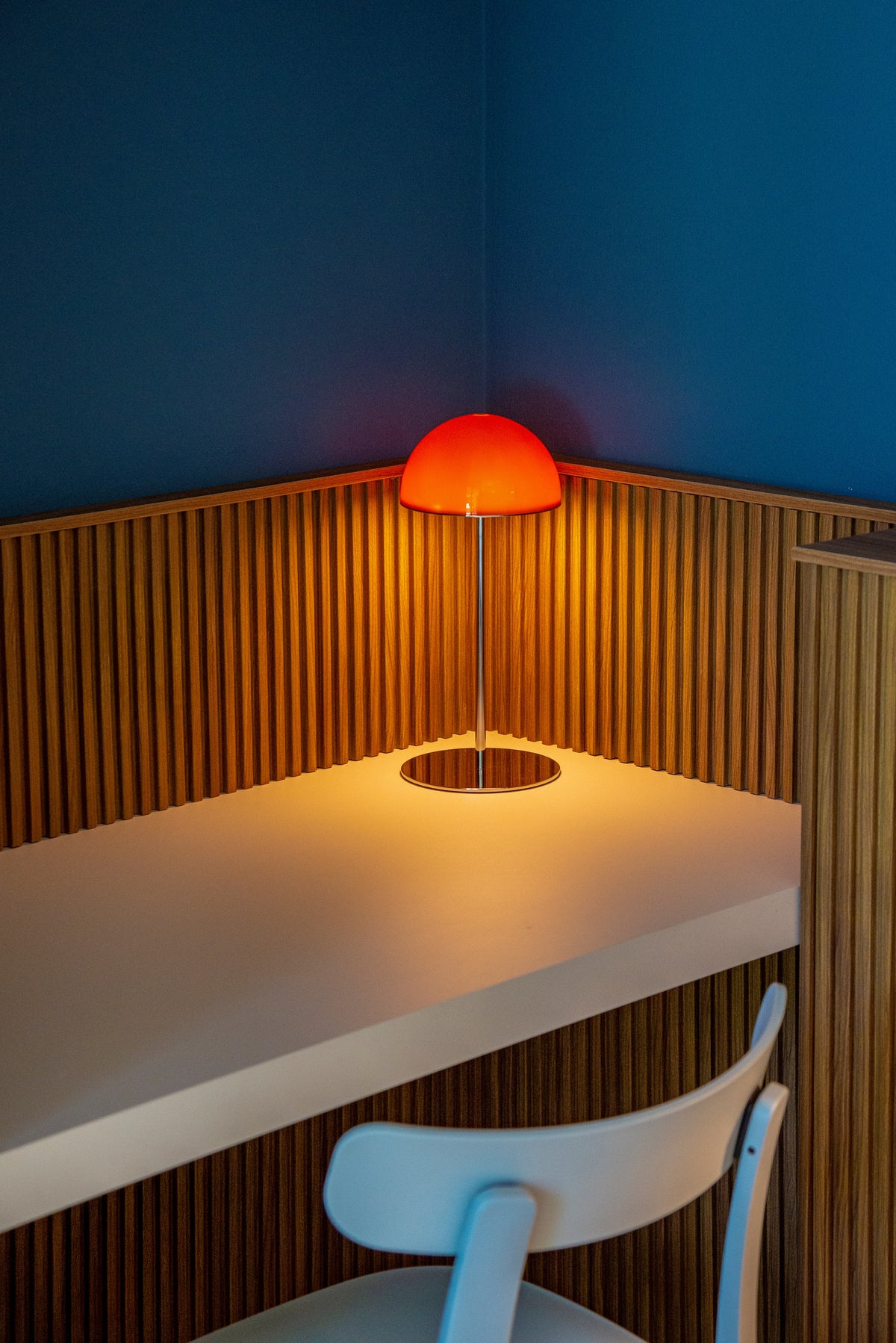 Dettaglio dello scrittoio con lampada arancione e boiserie in legno sulla parete blu