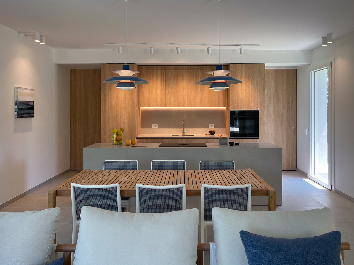 Zona giorno con cucina in legno, grande isola centrale e tavolo da pranzo, illuminata da sospensioni decorative