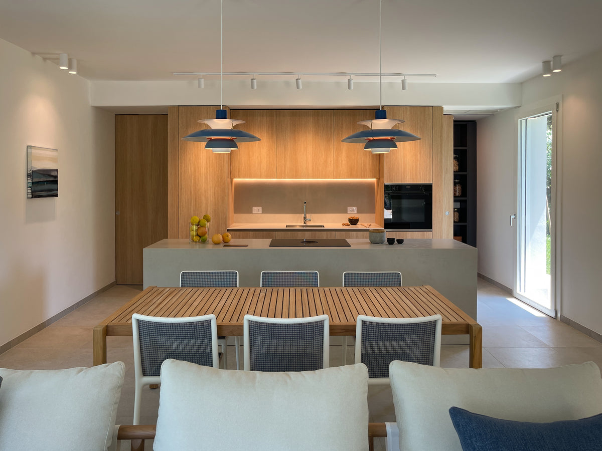Cucina con isola e zona pranzo in un ambiente luminoso, con arredi in legno e dispensa integrata nascosta