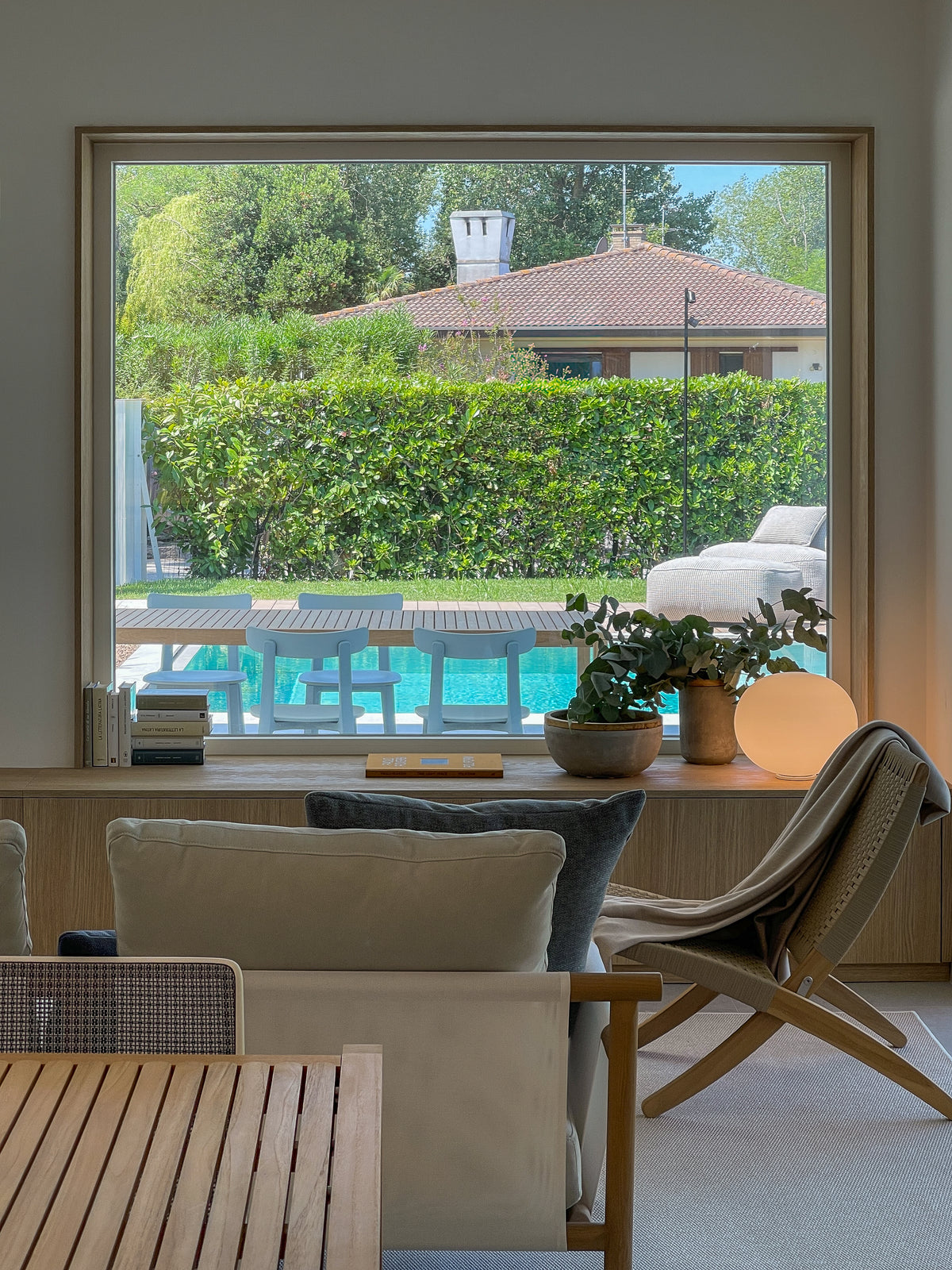 Zona relax con grande vetrata affacciata sulla piscina, sedute in legno e mobile contenitore sottofinestra