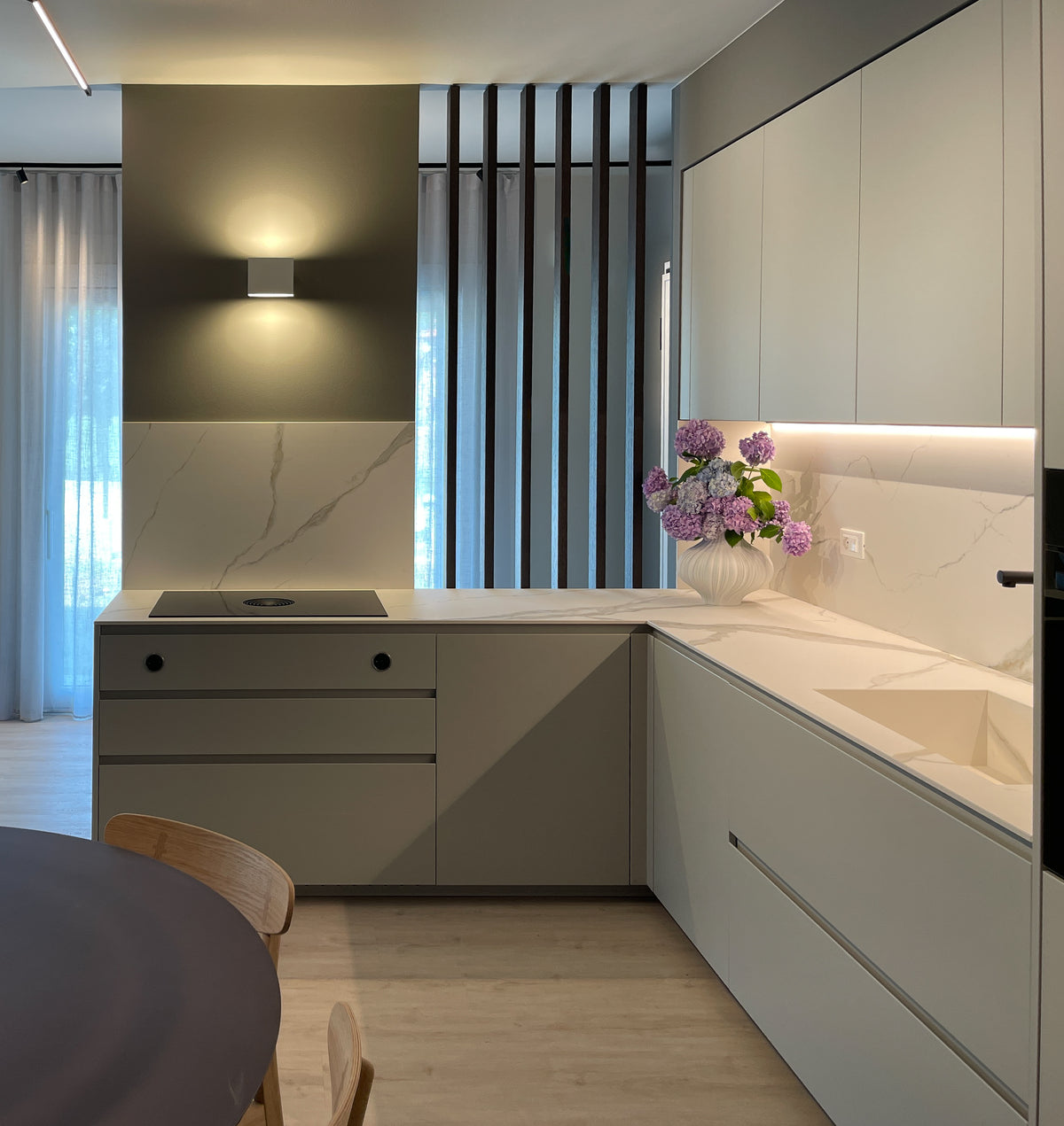 Cucina contemporanea su misura con penisola, piano effetto marmo, arredi chiari e divisorio verticale in legno tra cucina e ingresso