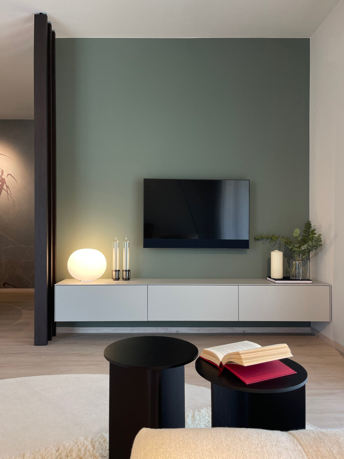 Dettaglio della parete TV verde con mobile sospeso bianco, tavolini neri e accessori decorativi