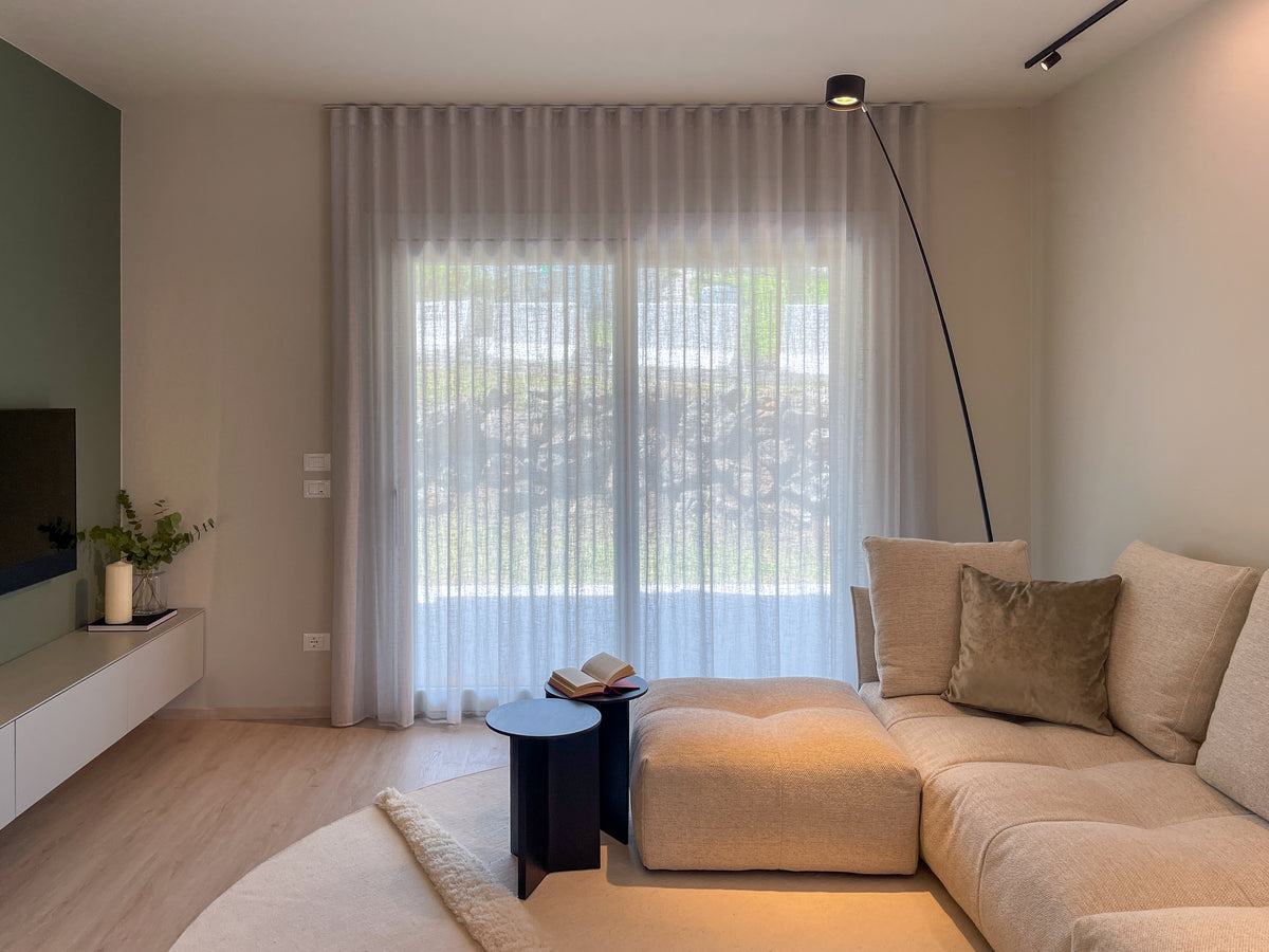 Zona living contemporanea con divano modulare chiaro, parete TV, grande vetrata e illuminazione ad arco