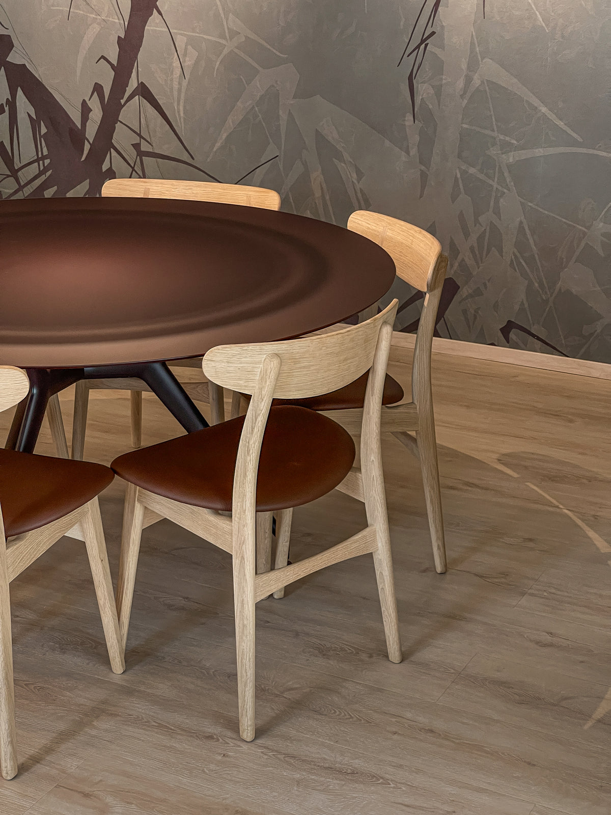 Dettaglio del tavolo da pranzo in vetro opaco color amaranto con sedie in legno chiaro e pelle