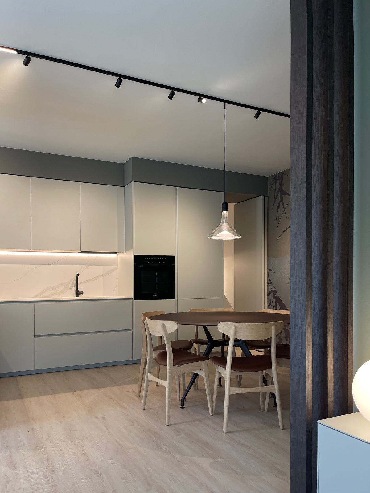 Dettaglio della zona pranzo con cucina su misura e tavolo rotondo, con listelli in legno decorativi e illuminazione a binario 