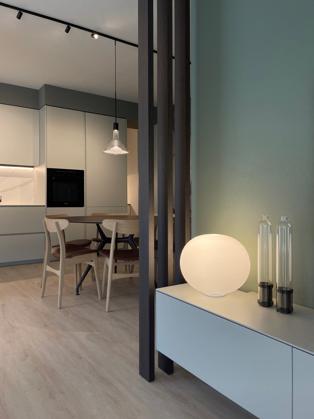 Dettaglio del mobile TV sospeso con lampada sferica e listelli in legno decorativi che separano la zona pranzo