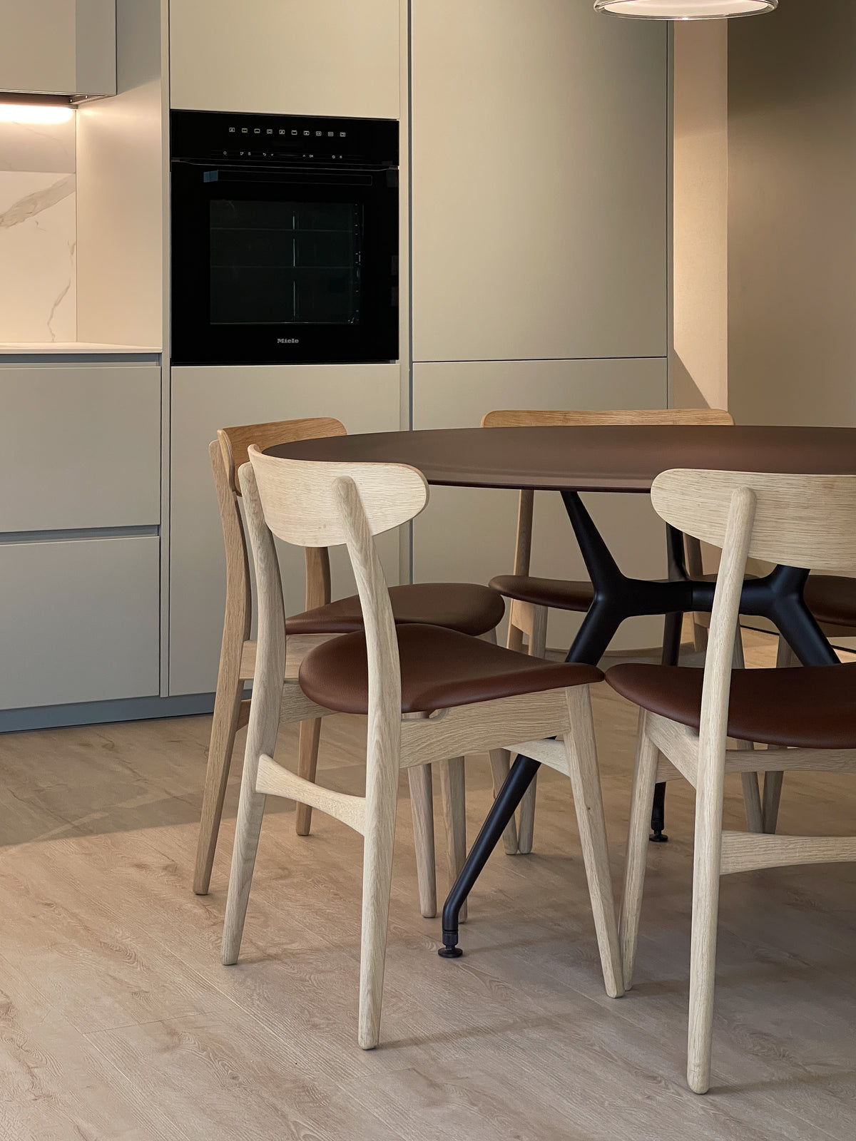 Dettaglio della zona pranzo con tavolo rotondo amaranto, sedie in legno e colonne forno della cucina