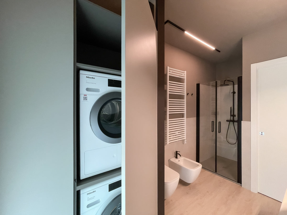 Progettazione bagno su misura con lavanderia integrata, doccia, sanitari sospesi e illuminazione a binario lineare