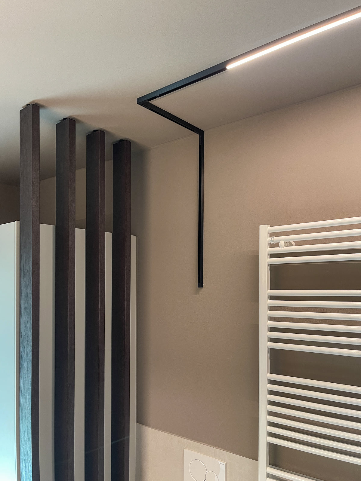 Dettaglio di progettazione bagno su misura con divisorio a listelli scuri, termoarredo bianco e luce a soffitto minimale a binario
