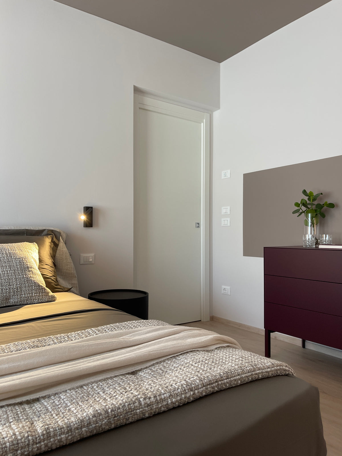 Interior design della camera matrimoniale con letto tessile, arredi su misura e accenti bordeaux