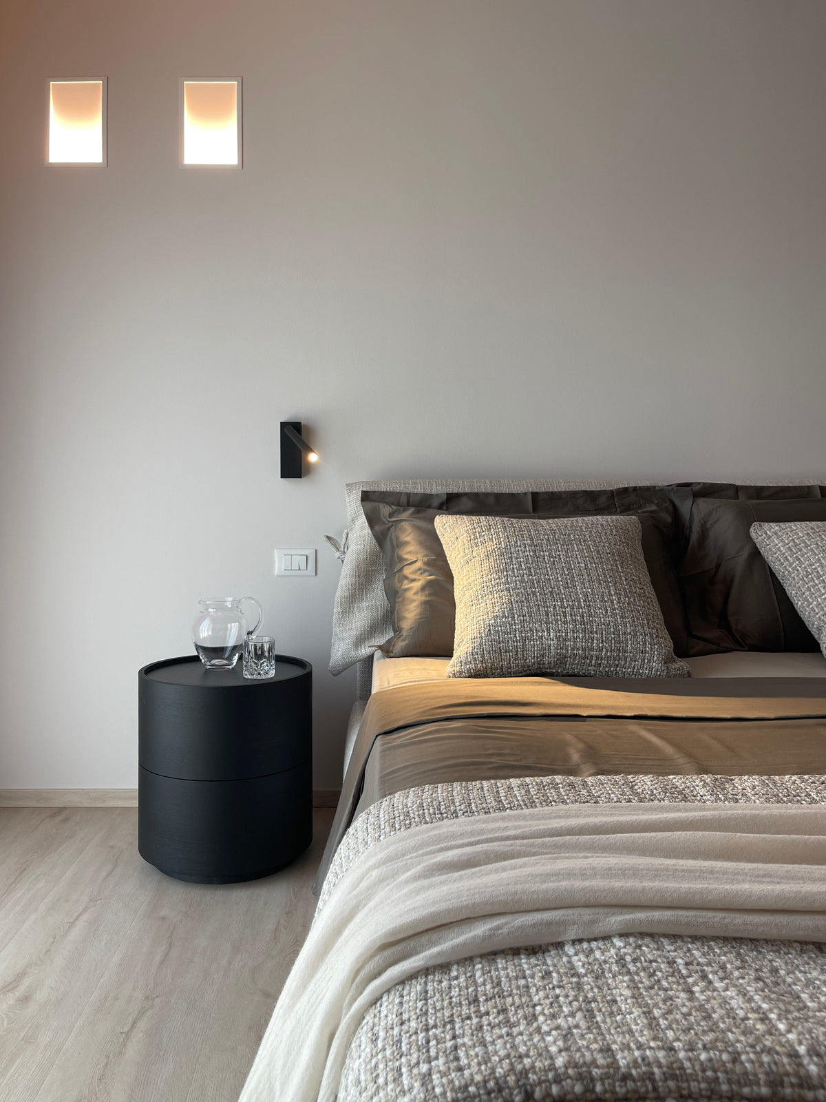 Camera padronale di nuova costruzione con letto imbottito, comodino rotondo nero e illuminazione a parete