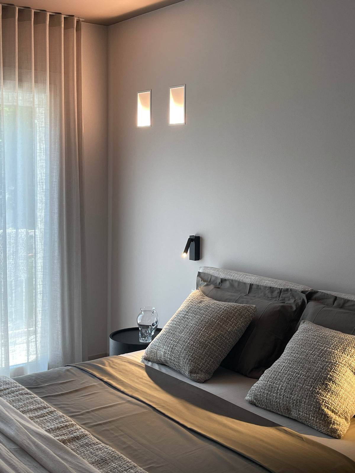 Interno camera matrimoniale con tende leggere a tutta altezza, letto tessile e illuminazione naturale