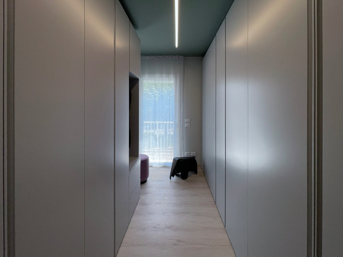 Progettazione su misura della cabina armadio con armadiature verde a tutta altezza, illuminazione lineare e pouf elefantino