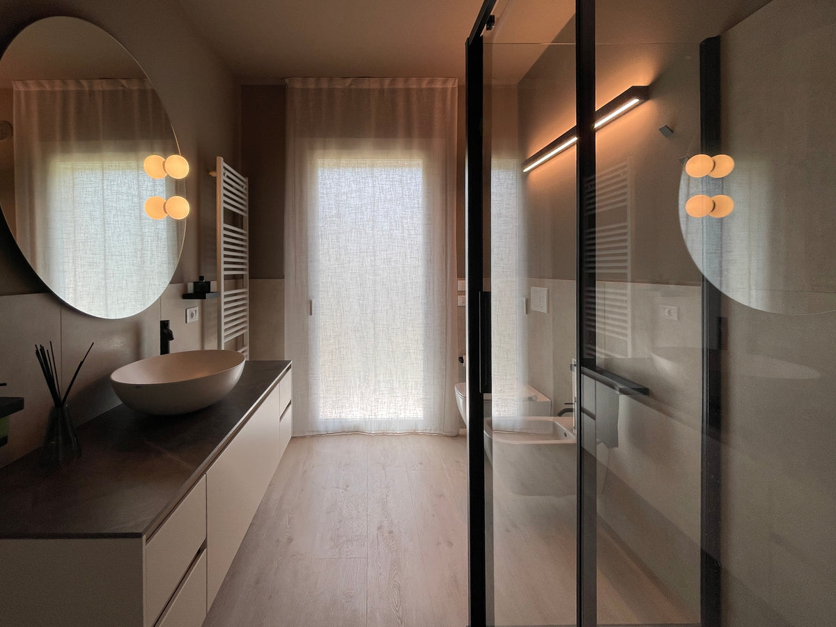 Bagno contemporaneo con doccia vetrata, lavabo da appoggio, grande specchio rotondo e finiture neutre