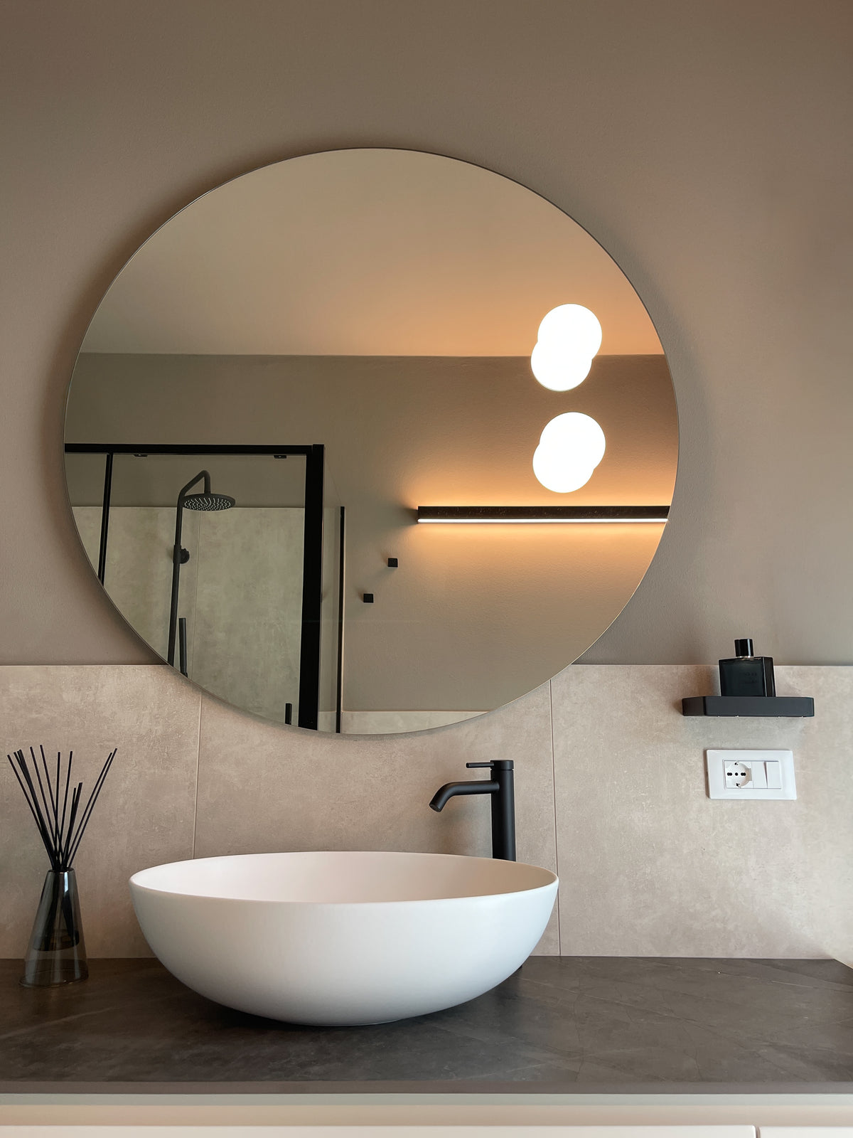 Dettaglio del progetto bagno su misura con lavabo da appoggio, rubinetteria nera, specchio rotondo e top effetto pietra