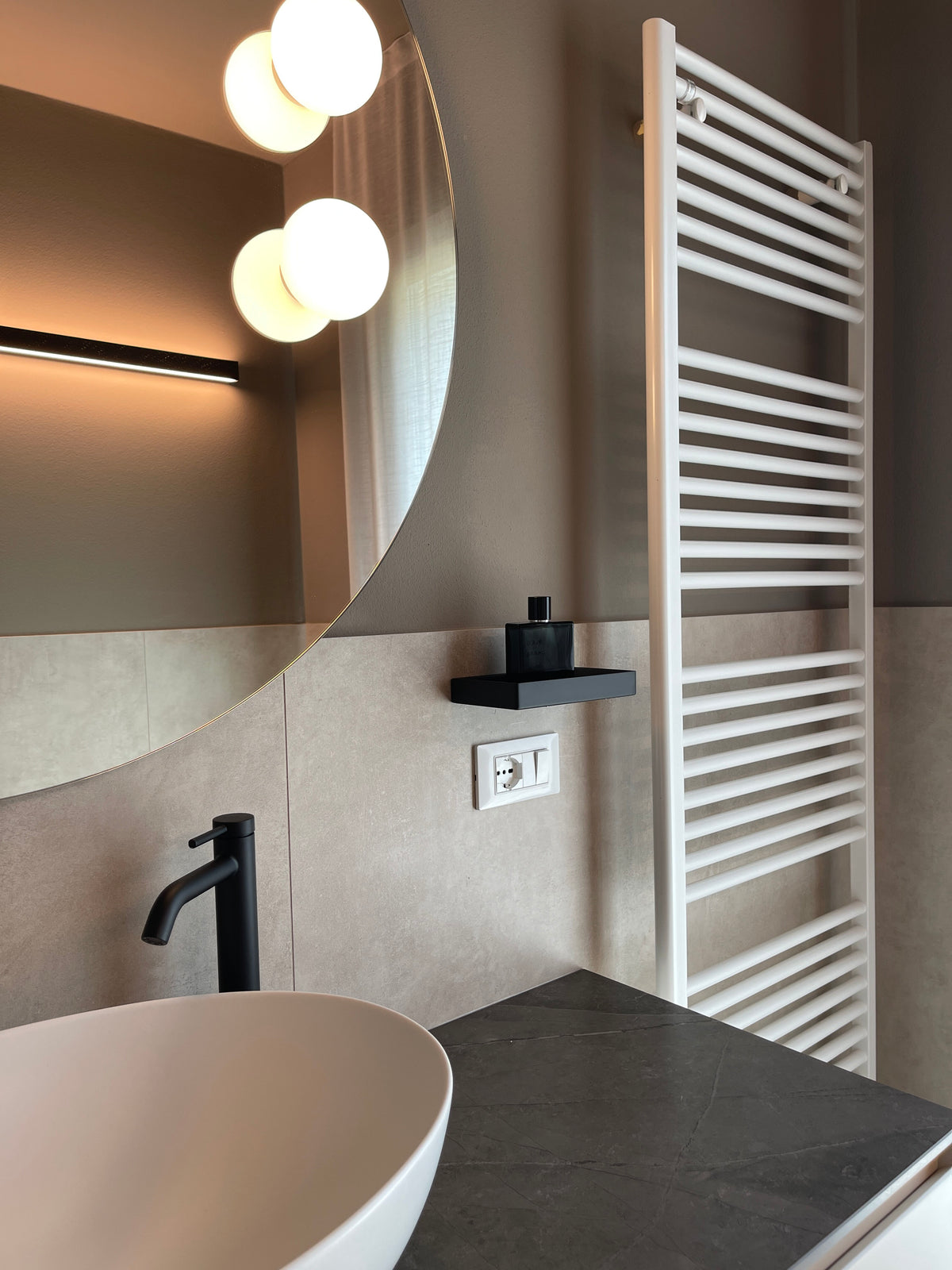 Bagno residenziale con lavabo da appoggio, specchio rotondo e rivestimento in gres chiaro