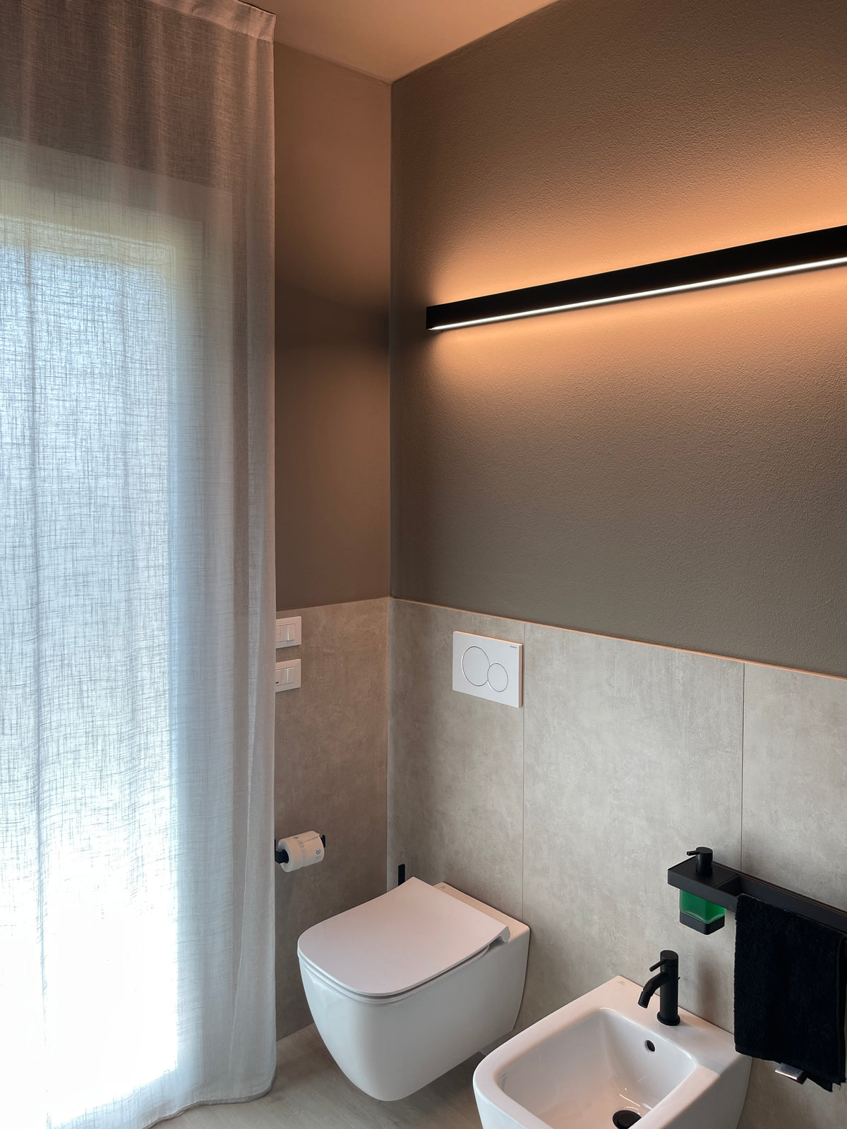 Bagno moderno in abitazione di nuova costruzione con sanitari sospesi, rivestimenti effetto pietra e illuminazione integrata