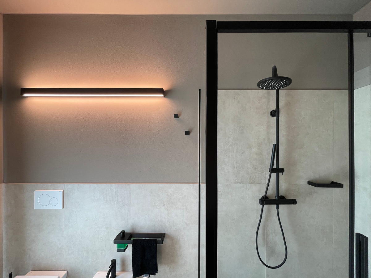 Interior design bagno con doccia, soffione nero, sanitari sospesi e illuminazione lineare su parete tortora