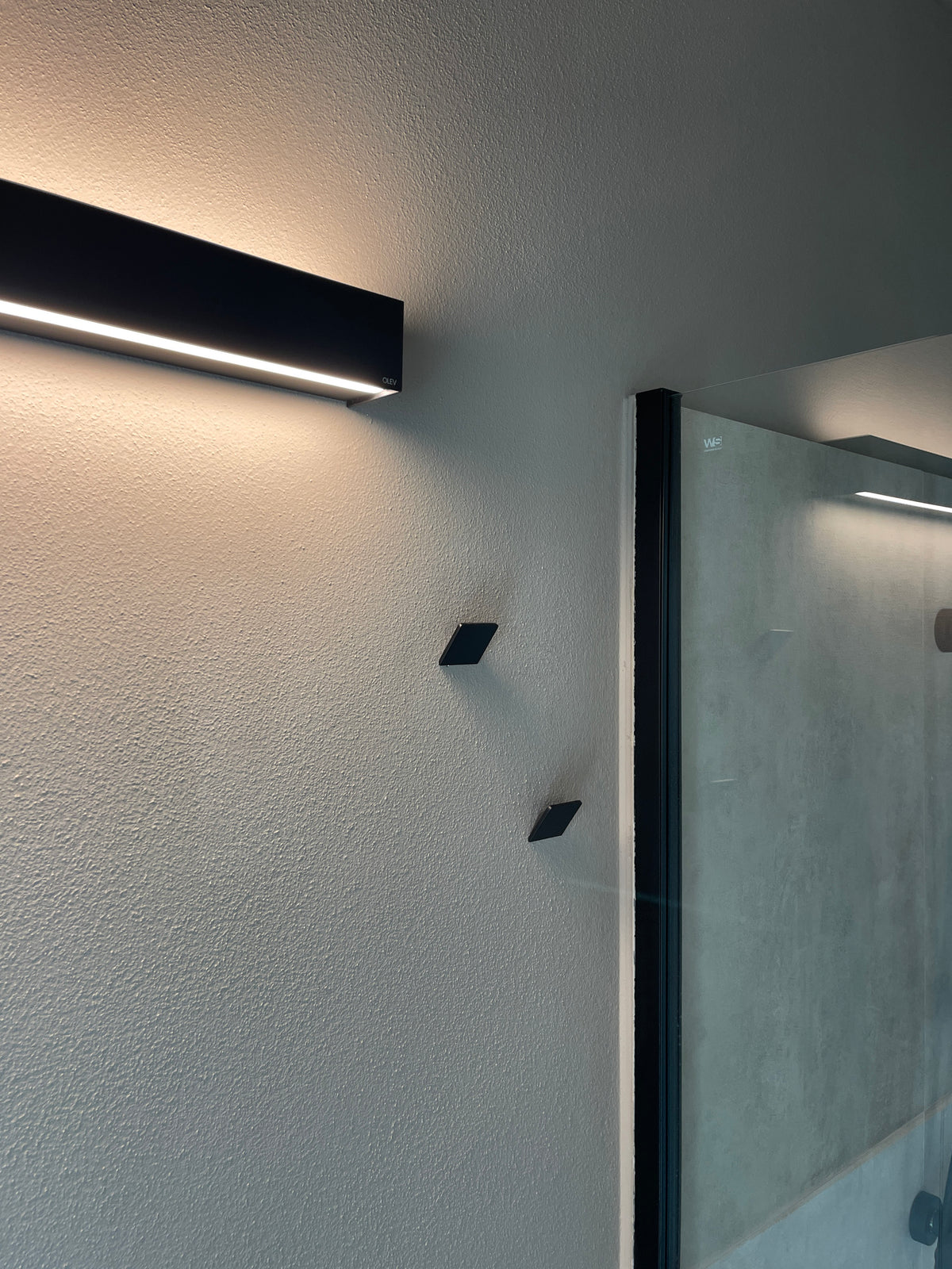 Dettaglio doccia bagno moderno con profilo nero, parete materica e luce lineare a parete