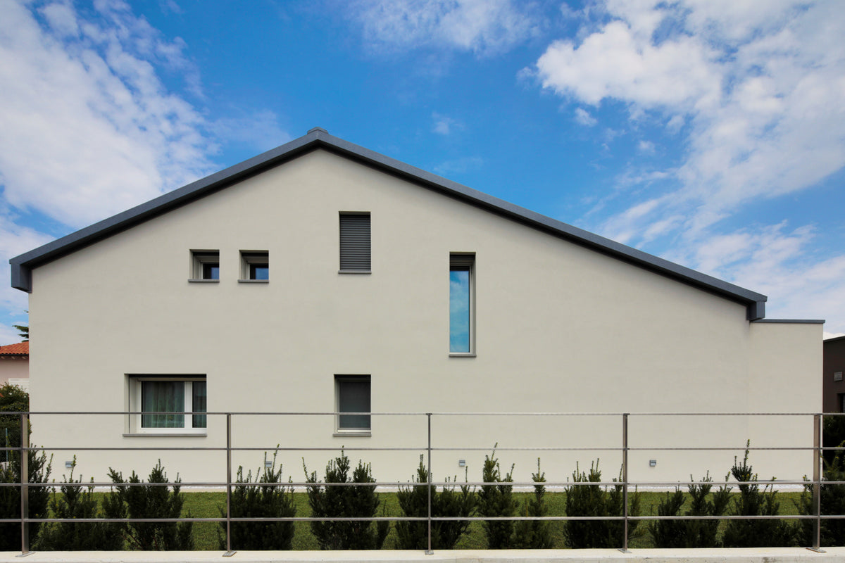 Facciata laterale della villa con intonaco chiaro, finestre irregolari e giardino perimetrale