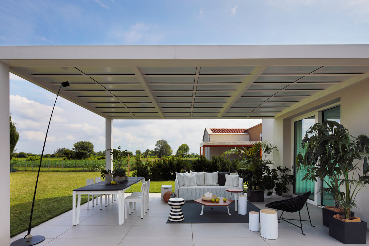 Pergola outdoor arredata come living esterno, con zona pranzo, divano chiaro e area relax, progettata per la convivialità