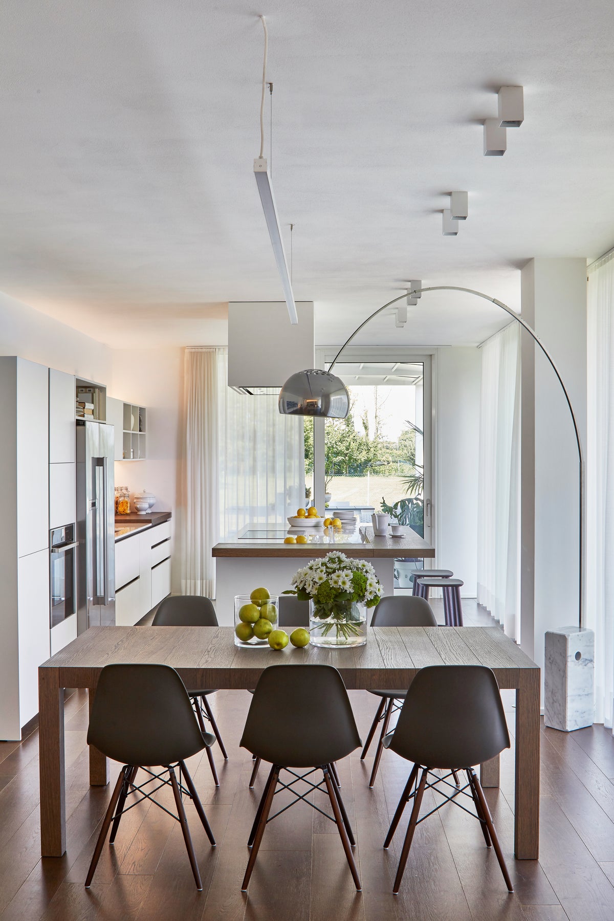 Sala da pranzo con tavolo in legno scuro, sedute nere e lampada da terra ad arco con base in marmo, in continuità con la cucina