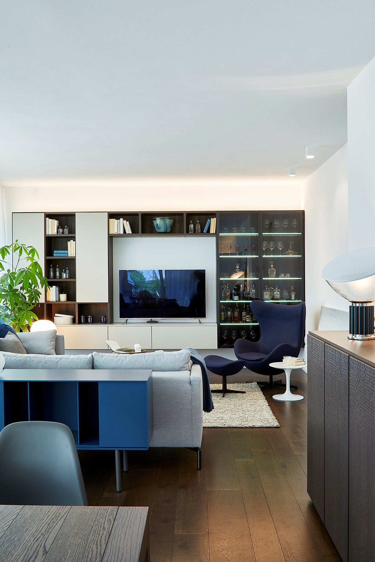 Living open space con divano chiaro, mobile contenitore blu e parete attrezzata in un intervento di interior design su misura