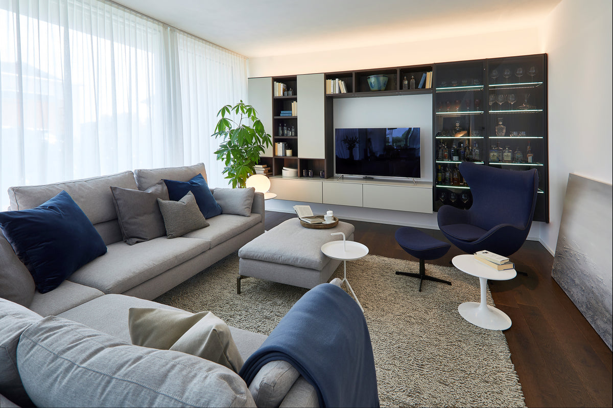 Zona relax con parete TV e vetrina illuminata integrata, tenda a tutta altezza e palette neutra con accenti blu