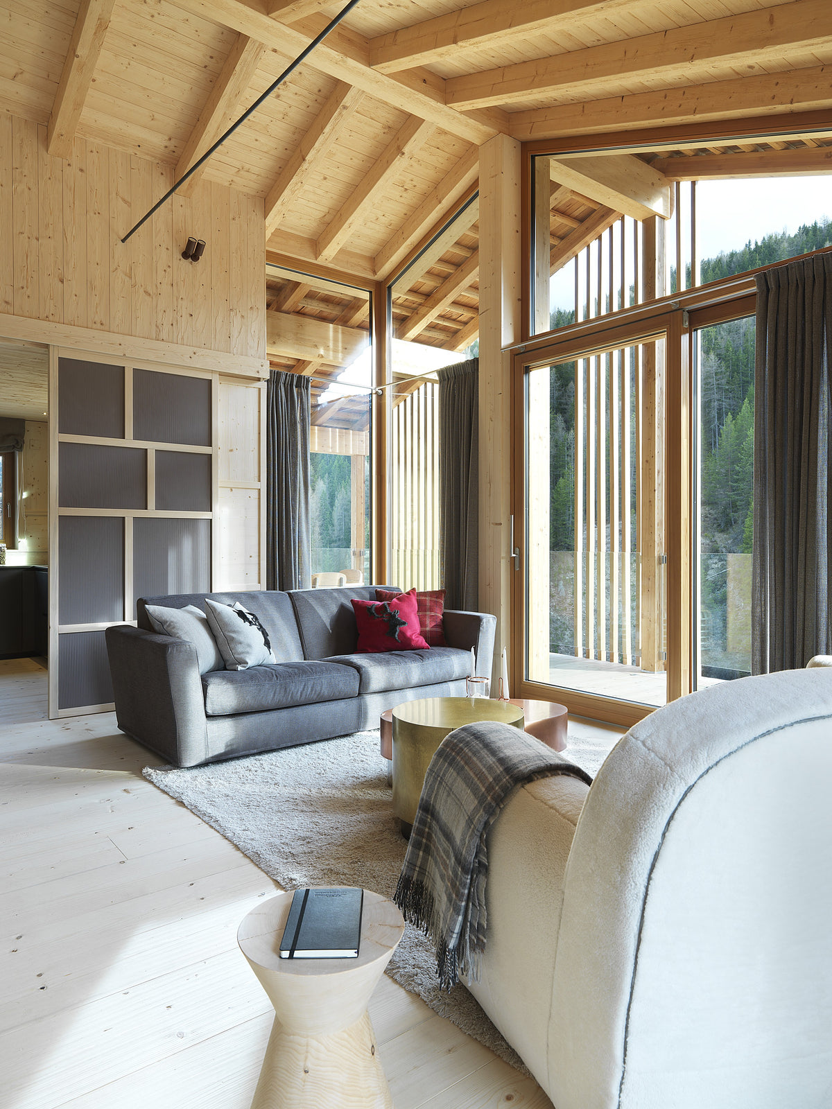 Zona living open space con divano grigio, arredi su misura e boiserie in legno chiaro in stile alpino moderno