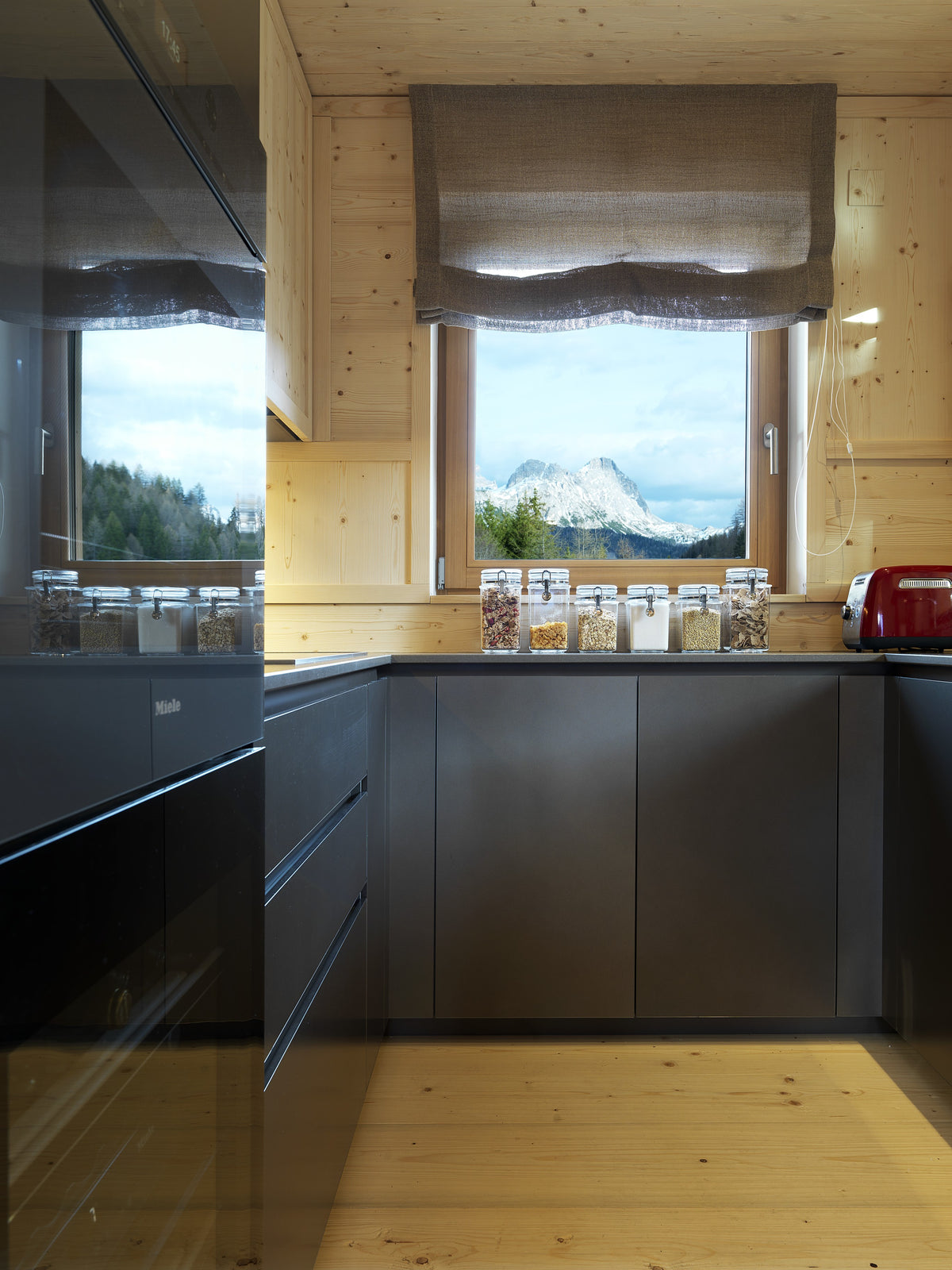 Cucina lineare con vista sulle montagne, superfici scure a contrasto con il legno chiaro