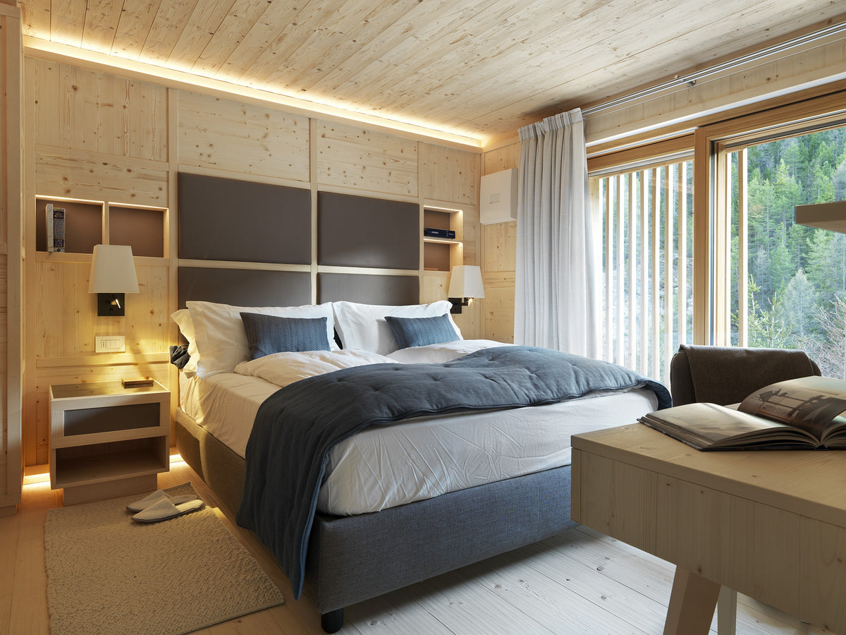 Camera da letto con boiserie in legno e finestra panoramica, con palette neutra e design discreto coerente con il contesto montano