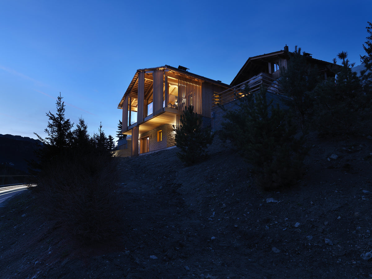 Vista esterna dello chalet illuminato inserito nel paesaggio alpino, in equilibrio tra tradizione e linguaggio attuale