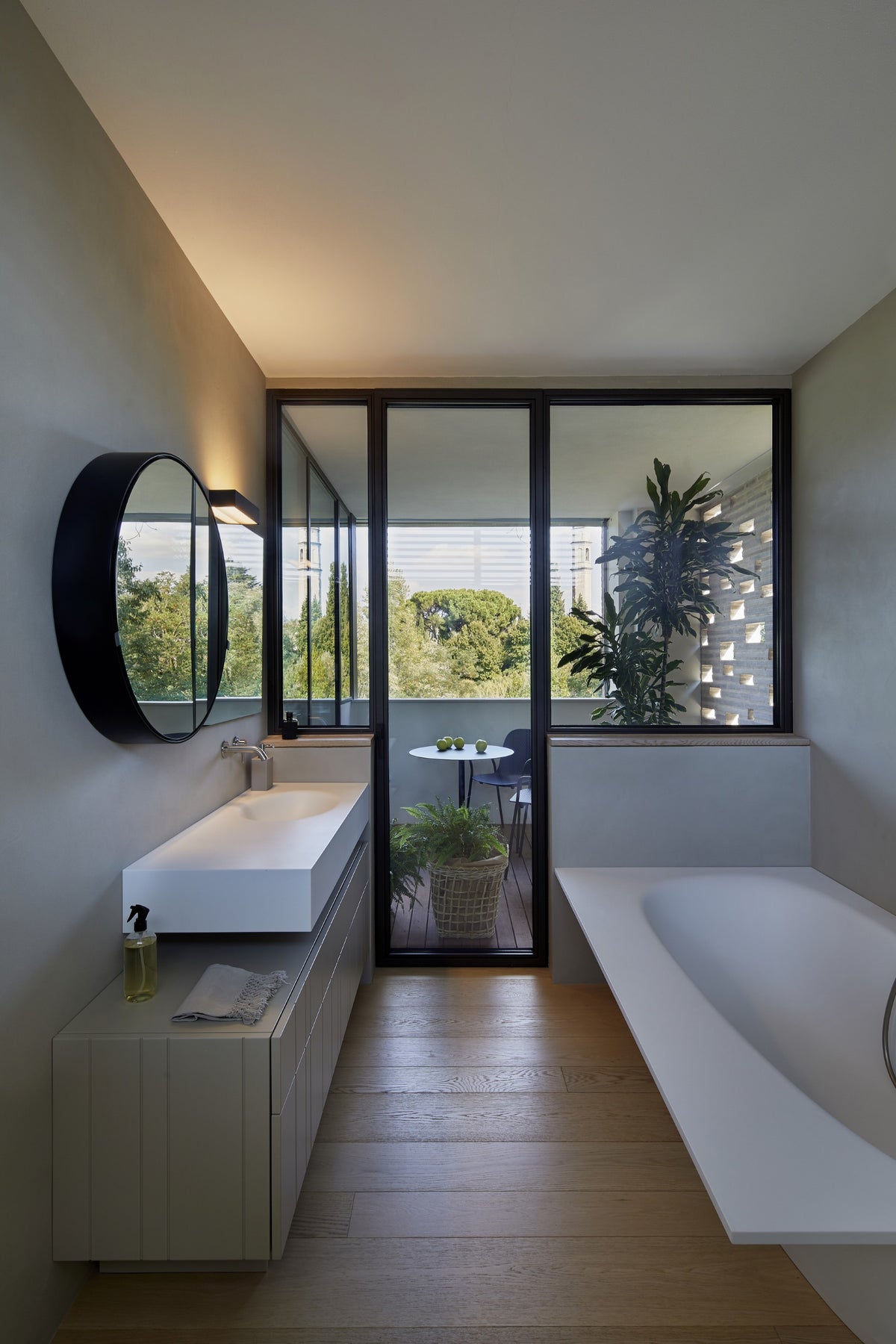 Bagno con lavabo sospeso, specchio rotondo e vasca affacciata sulla vetrata verso il terrazzo