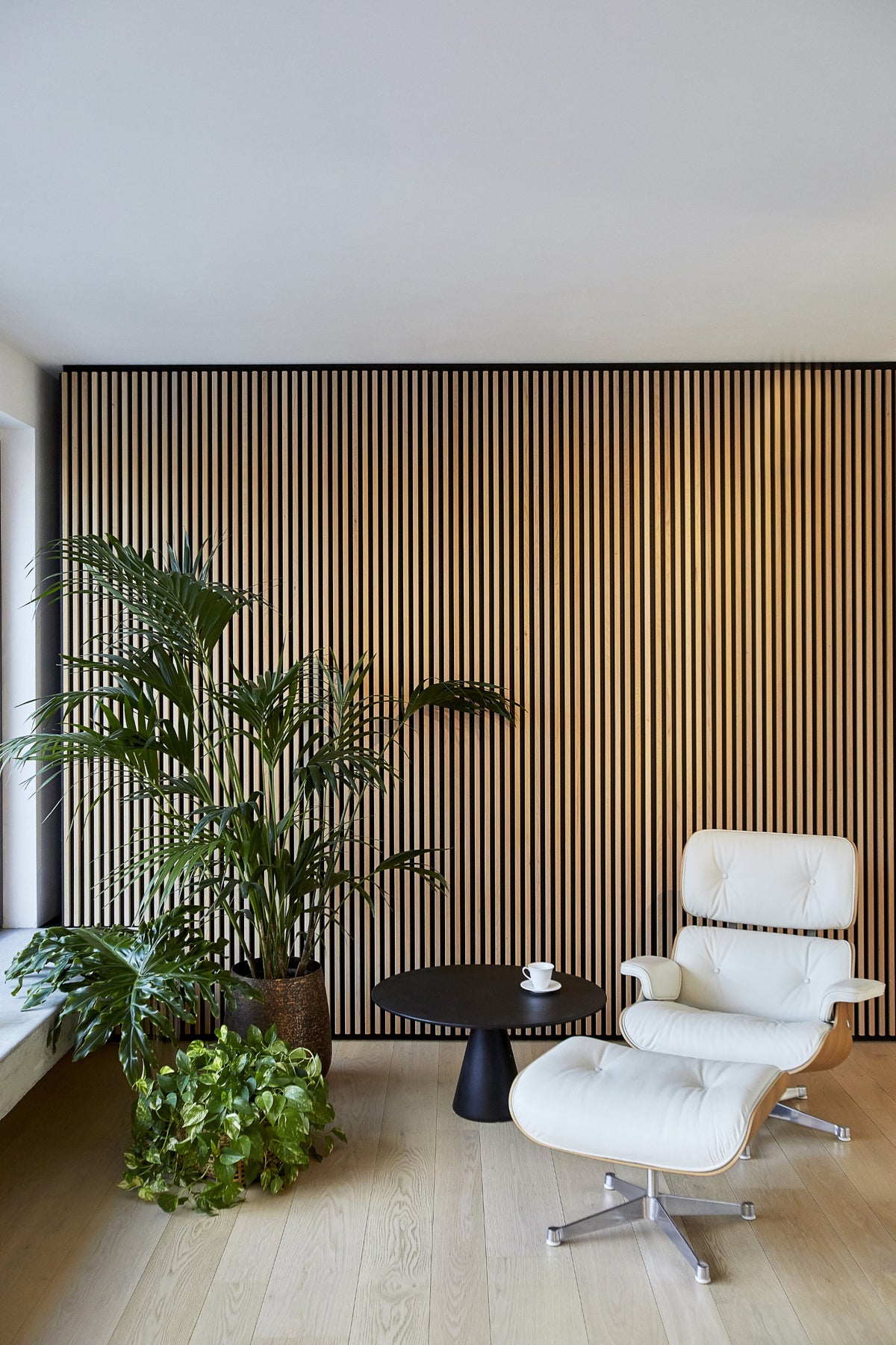 Angolo relax con poltrona bianca Eames Lounge, parete in legno e luce naturale